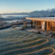 Maison contemporaine au lever du jour, gelée blanche sur la pelouse et tracé du capteur géothermique horizontal visible dans le terrain, module de pompe à chaleur NEXTHERM dans la pièce vitrée