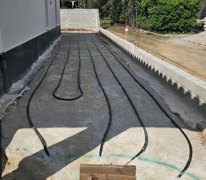 Boucles de capteurs géothermiques en attente de raccordement le long d’un mur, chantier Kraft Géothermie